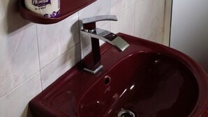 Ein Badezimmer mit einem runden Spiegel, einem roten Waschbecken und einem Toilettenpapierhalter mit einem Rollen Nivea Extra Mild Toilettenpapier.