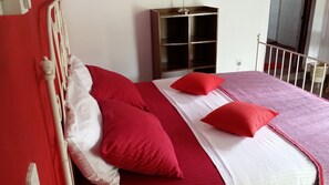 A bed with red and white bedding, a wooden headboard, and a small bedside table. - Village Villa Home Stay (Kandy)