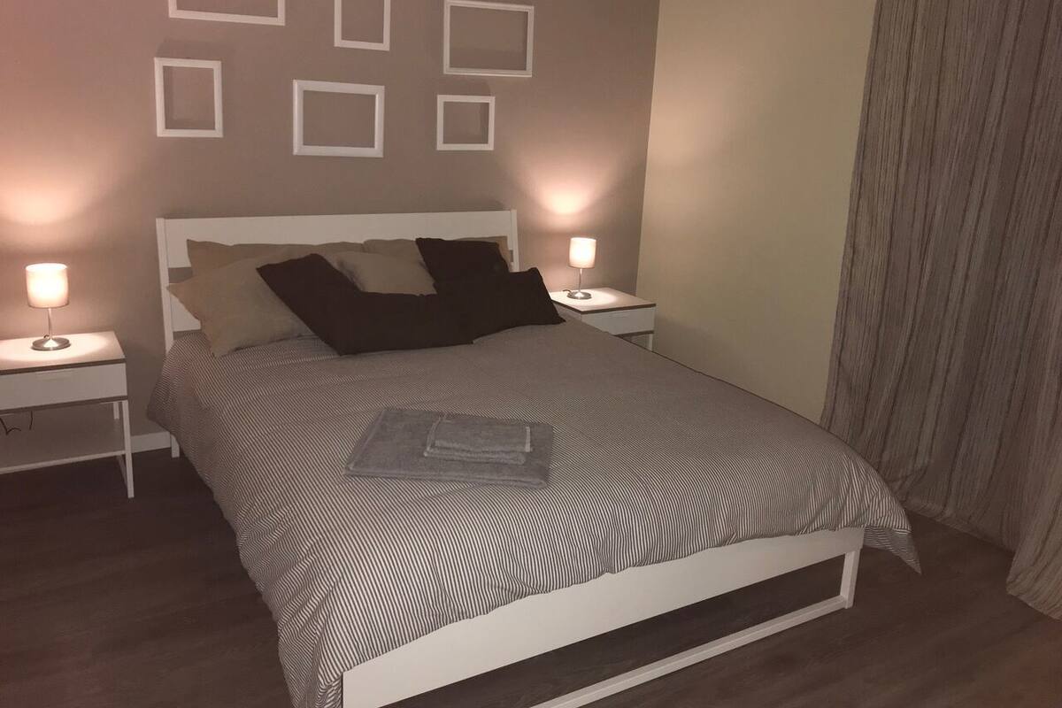 A neatly made bed with a striped bedspread, two bedside tables with lamps, and a wall with several empty picture frames.