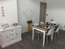 Un'area pranzo con un tavolo in legno e sedie bianche, un armadietto bianco con cassetti e una pianta in vaso.