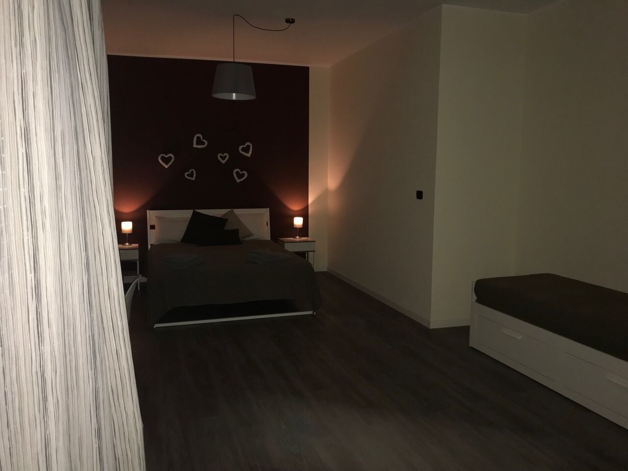 Un dormitorio con cama, mesitas de noche, una lámpara colgante y un banco.