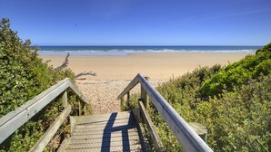 Una escalera de madera que lleva a una playa, con vistas claras al océano.