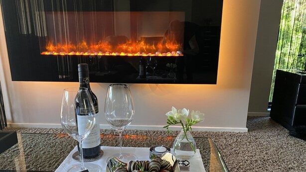 Una mesa con una botella de vino, dos copas, un florero con flores y fresas bañadas en chocolate.