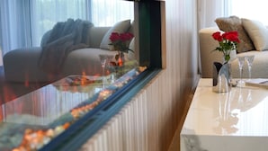 Una sala de estar moderna con una mesa de centro de vidrio, un sofá con una manta y un jarrón con rosas rojas.