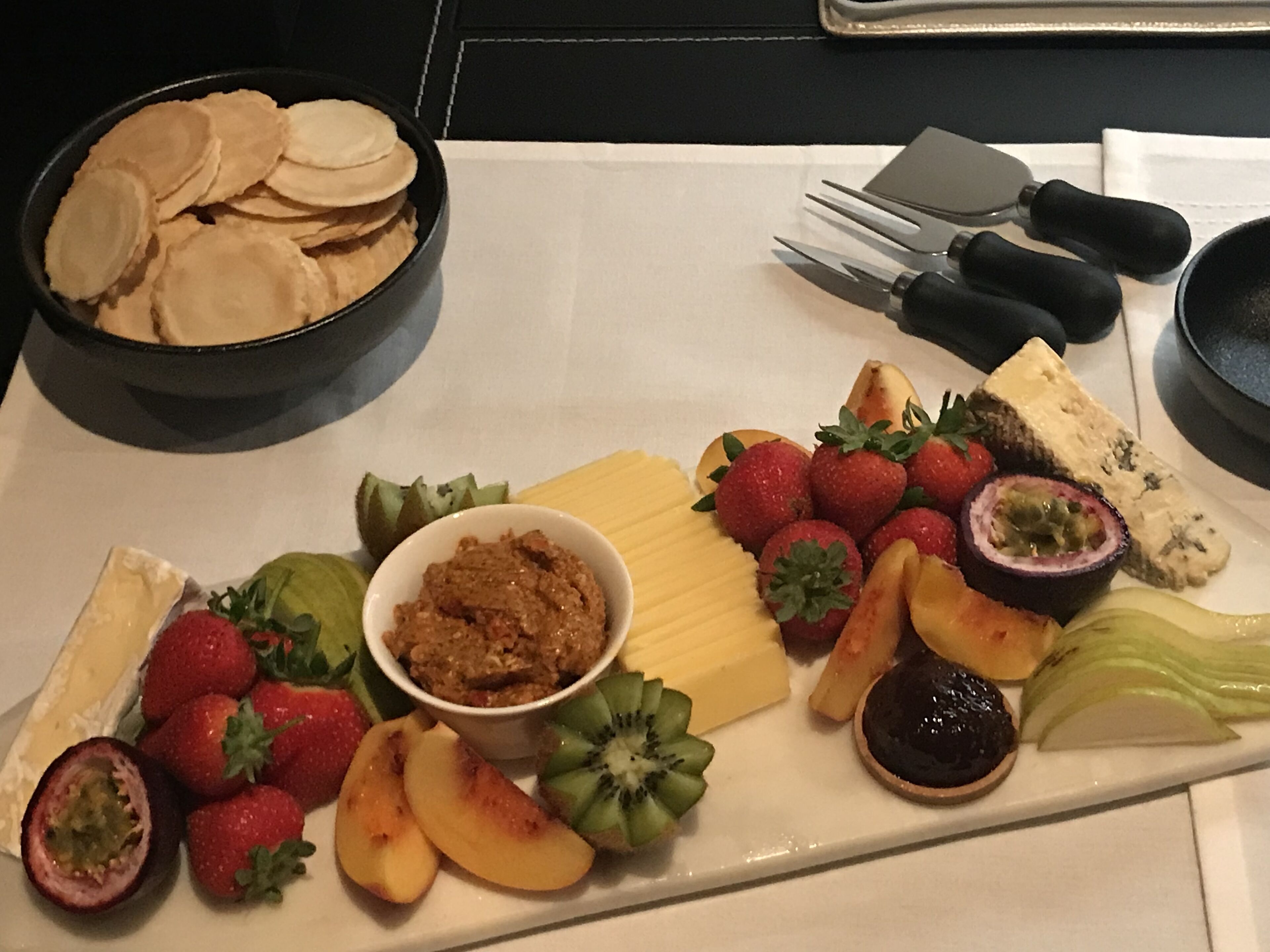 Una bandeja con frutas variadas, queso y un recipiente de salsa.