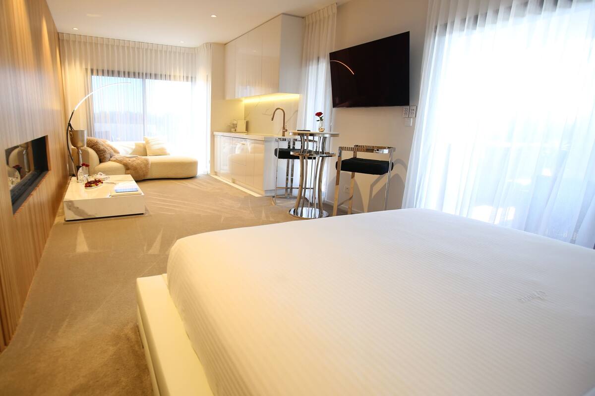 Quarto de hotel moderno com uma cama grande, um sofá, uma escrivaninha e uma televisão.