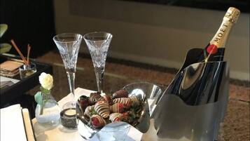 A table with a bottle of Moët champagne, two crystal glasses, a bowl of chocolate-covered strawberries, and a small vase with a white rose.