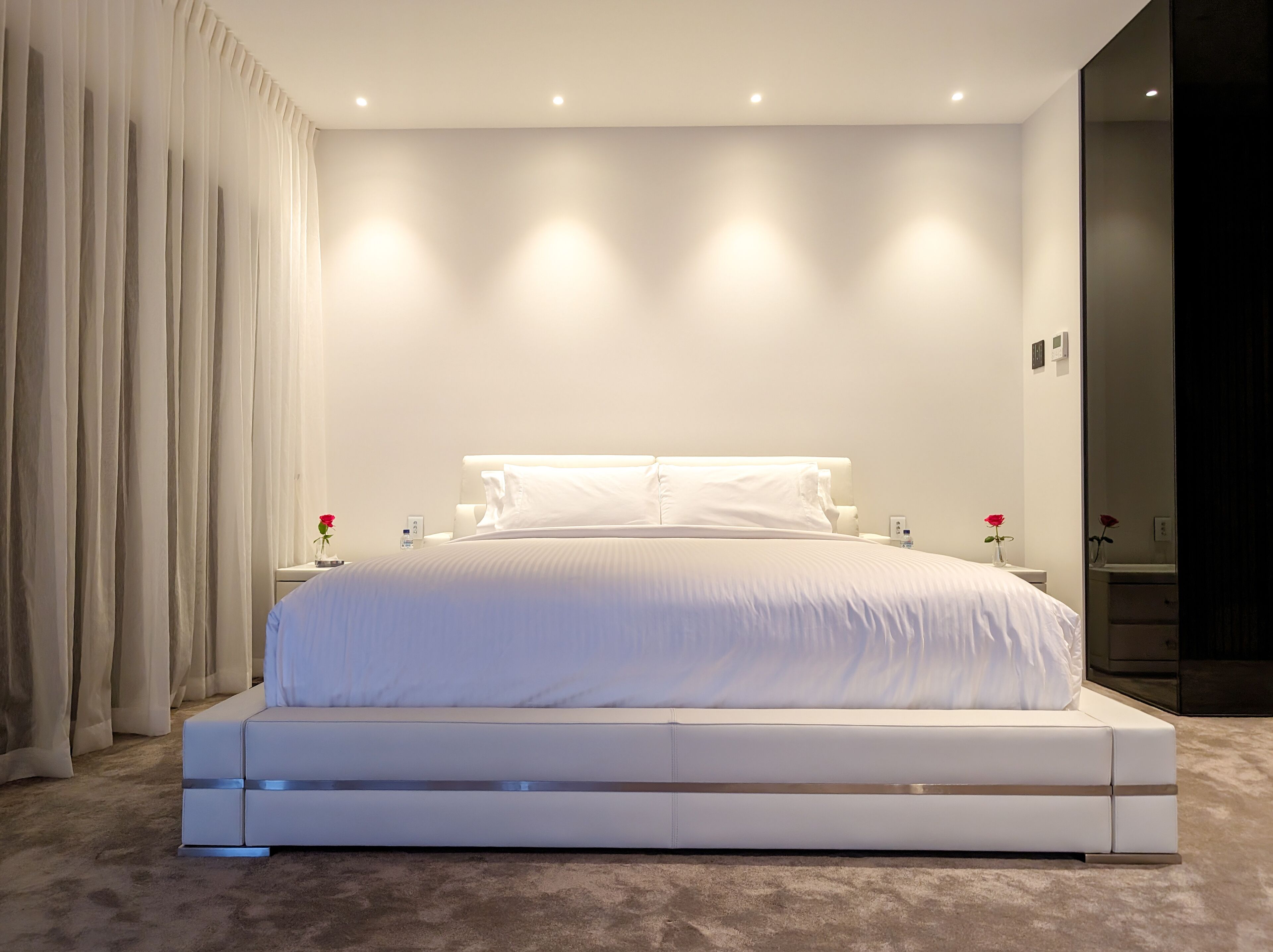A modern bedroom with a large bed, white linens, and a minimalist design.