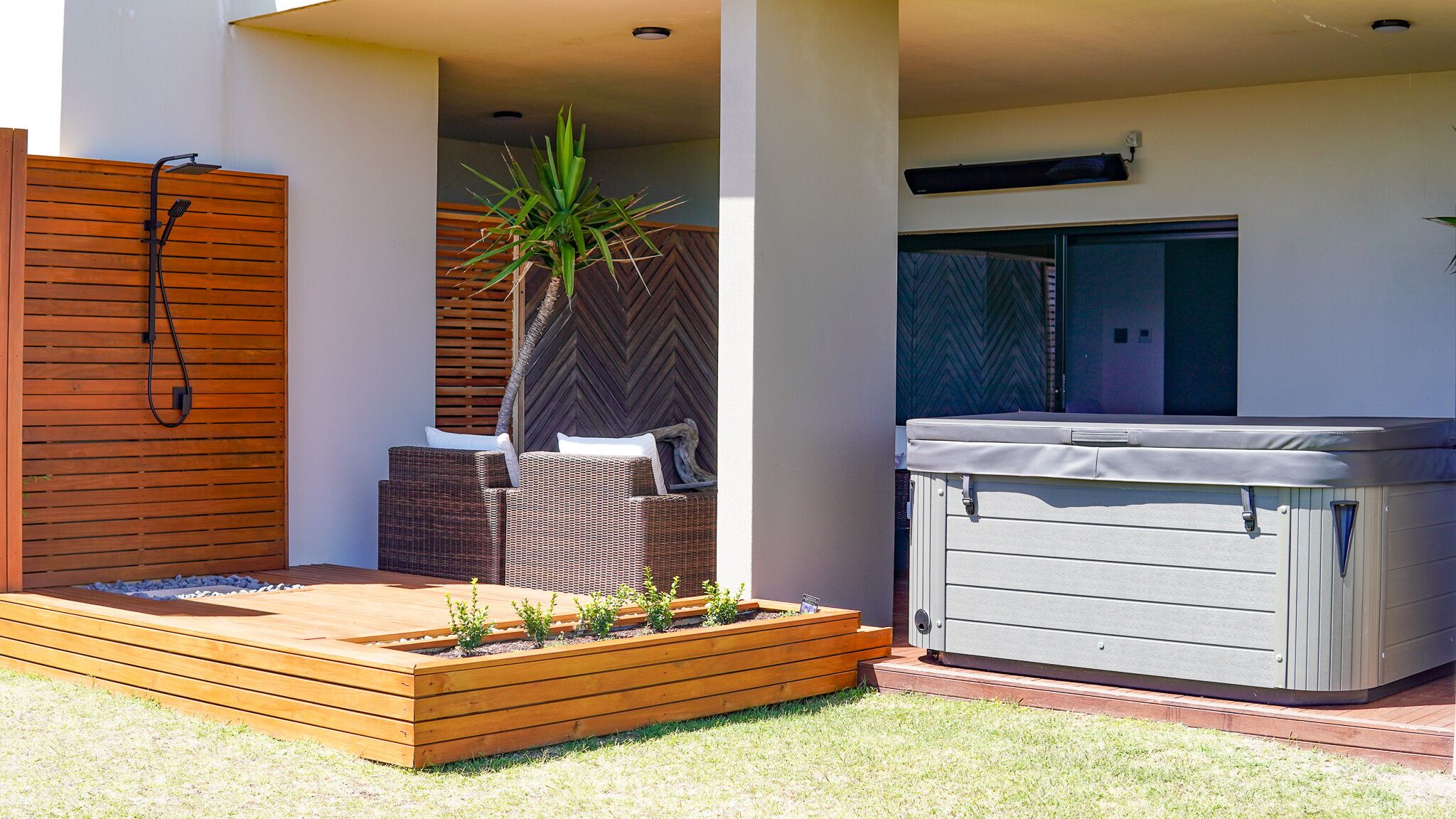 Un patio exterior moderno con jacuzzi, terraza de madera y zona de estar con una planta.