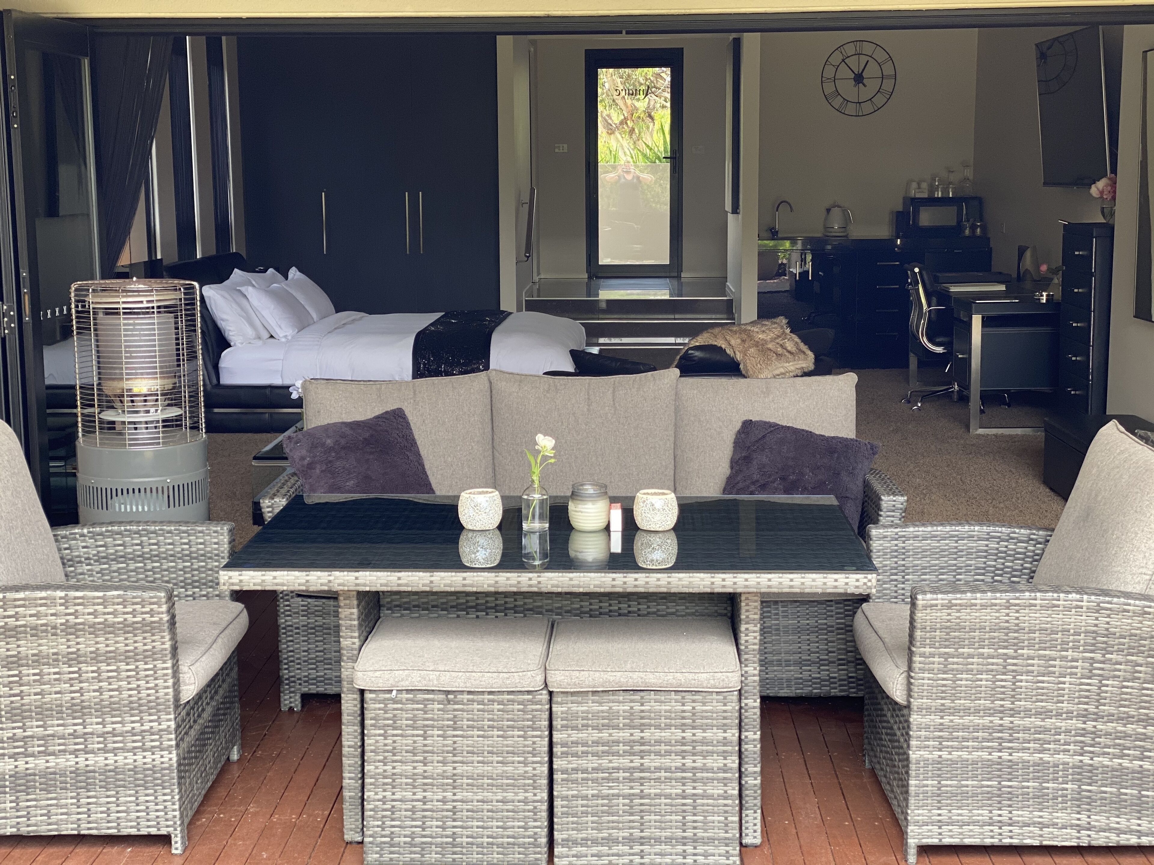 A modern living area with a sofa, a dining table, wicker furniture, and a kitchen area with a microwave and sink.