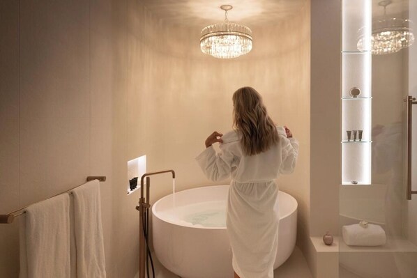 A woman in a white robe standing in a large bathtub with a chandelier above. - Amaré Beachside Luxury (Turners Beach)
