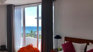 Een hotelkamer met een bed, nachtkastje, lamp en uitzicht op de oceaan door grote ramen.