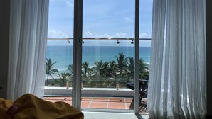 Ein Zimmer mit großem Fenster, Blick auf einen Strand mit Palmen und das Meer.