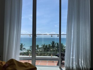 A room with a large window overlooking a beach with palm trees and the ocean. - Araliya OceanFront Condos Nilaveli (Nilaveli)