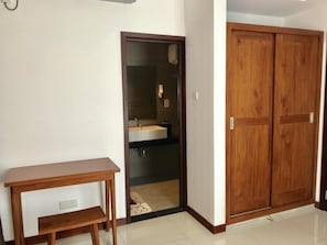 A room with a wooden desk, a wardrobe, and a bathroom visible through an open door.
