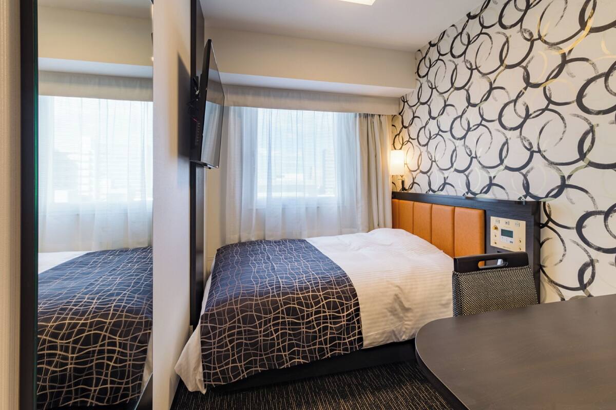 A hotel room with two beds, a TV, a desk, and a patterned wall.