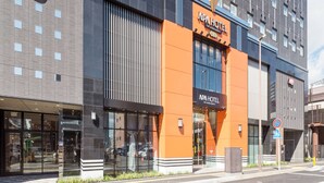 Un edificio moderno con una fachada llamativa en naranja y negro, que muestra un cartel de "APA HOTEL" y una entrada visible.