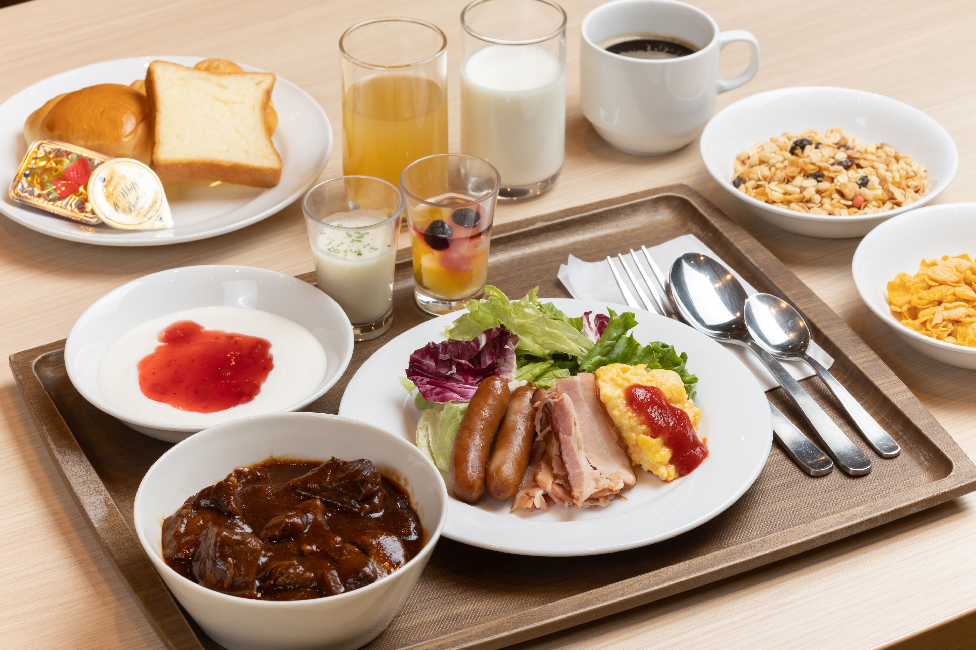 Bandeja de desayuno con diversos alimentos como tostadas, salchichas, huevos y una ensalada.