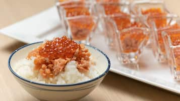 A bowl of rice topped with salmon roe and a plate of small glasses containing salmon roe.