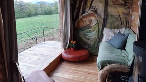 Ein gemütliches Blockhaus-Interieur mit Holzboden, einer Couch mit Kissen, einem roten Hocker und einem Baumgemälde an der Wand.