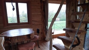 Ein rustikaler Holzraum mit einem runden Holztisch und Bänken, einer Treppe mit Metallgeländern sowie Blick auf Grünflächen au ßerhalb.
