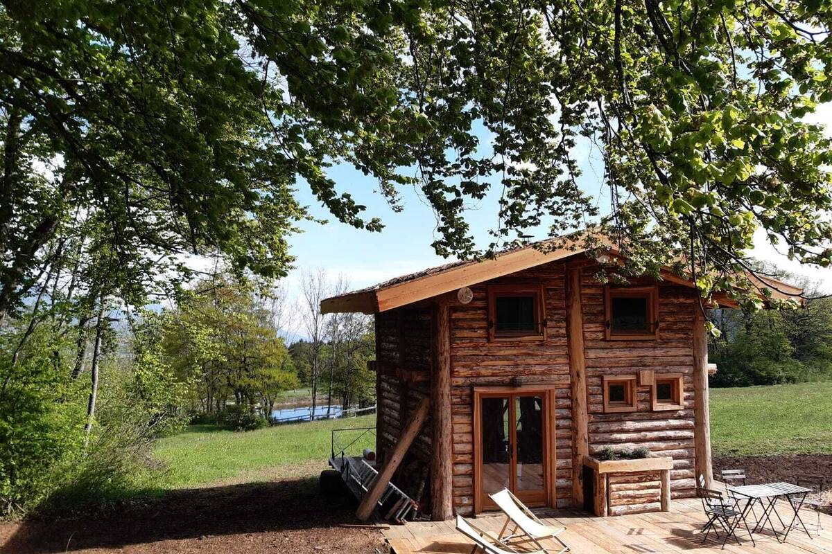 Una cabaña rústica de troncos con una terraza de madera, un espacio de estar cubierto al aire libre y vistas a un paisaje natural.