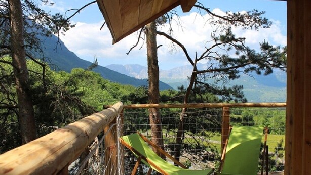 Eine Holzterrasse mit einer Hängemattenliege und einem Hollerker, mit Blick auf eine gebirgige Landschaft.