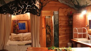 Ein gemütliches Blockhaus-Zimmer mit Holzvertäfelung, einem Bett mit floralem Vorhang, einer Holzbank und einer kleinen Küchenzeile mit Spüle.