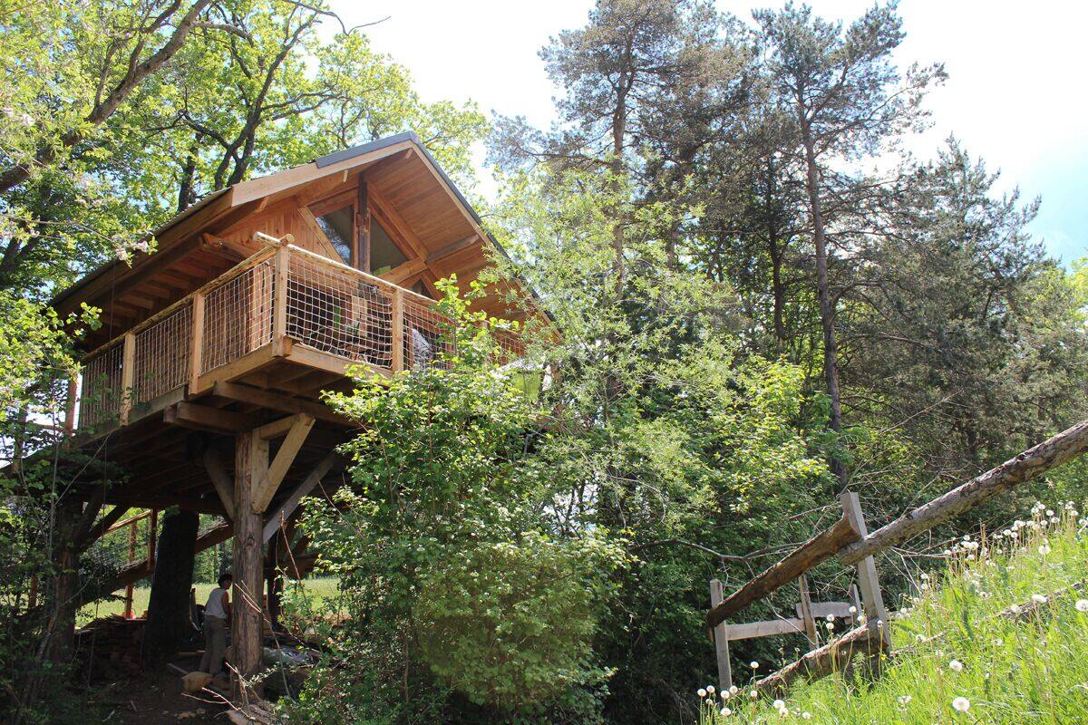 Una casa en los árboles con fachada de madera y un balcón, rodeada de un bosque frondoso.