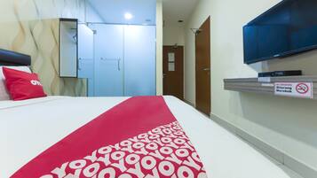 A hotel room with a bed, a red and white patterned bedspread, a television mounted on the wall, and a no smoking sign.