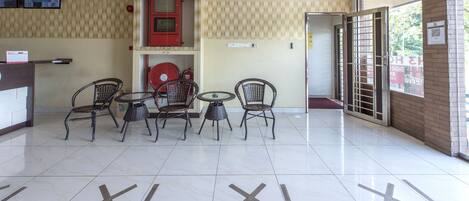 A lobby with a reception desk, three wicker chairs around a small table, a clock, and a red cabinet.