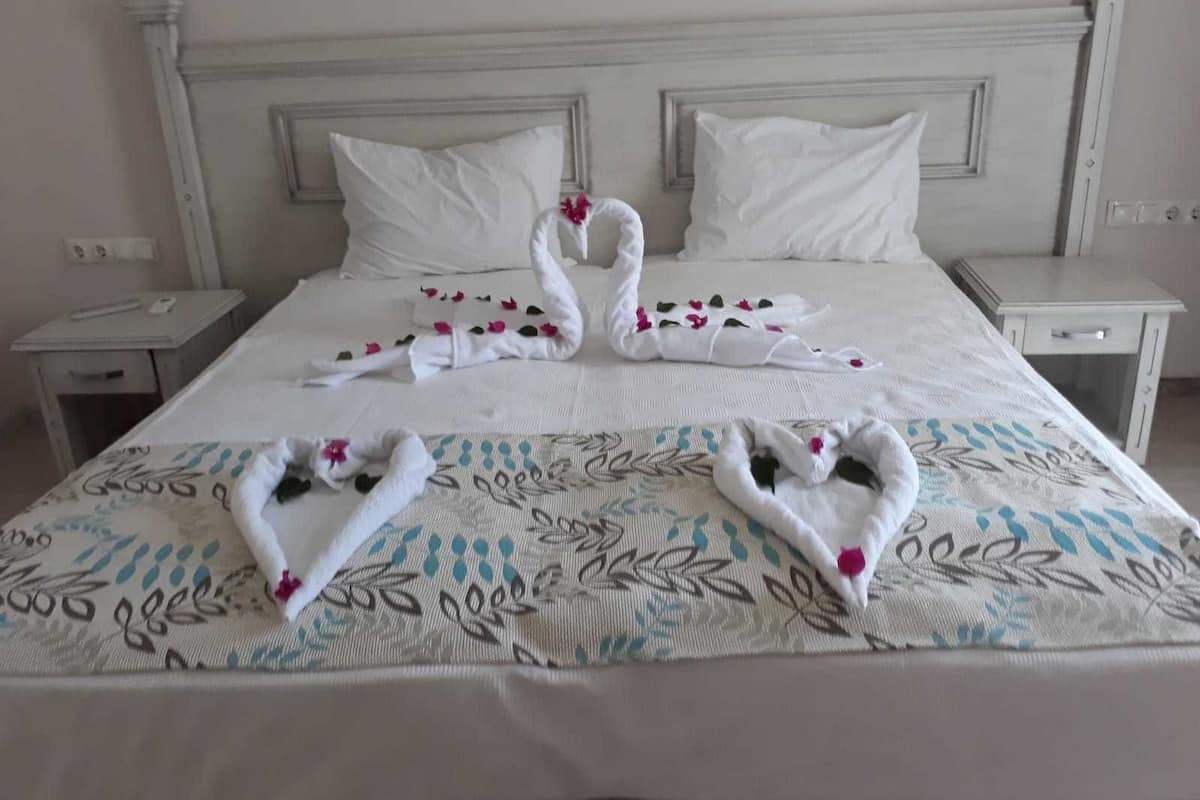Quarto de hotel com uma cama grande, cabeceira branca e duas mesas de cabeceira.