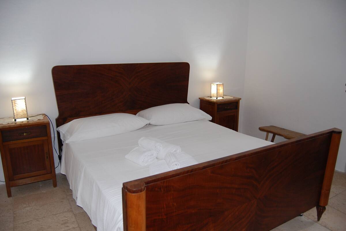 A wooden bed with white linens and two bedside tables with lamps.