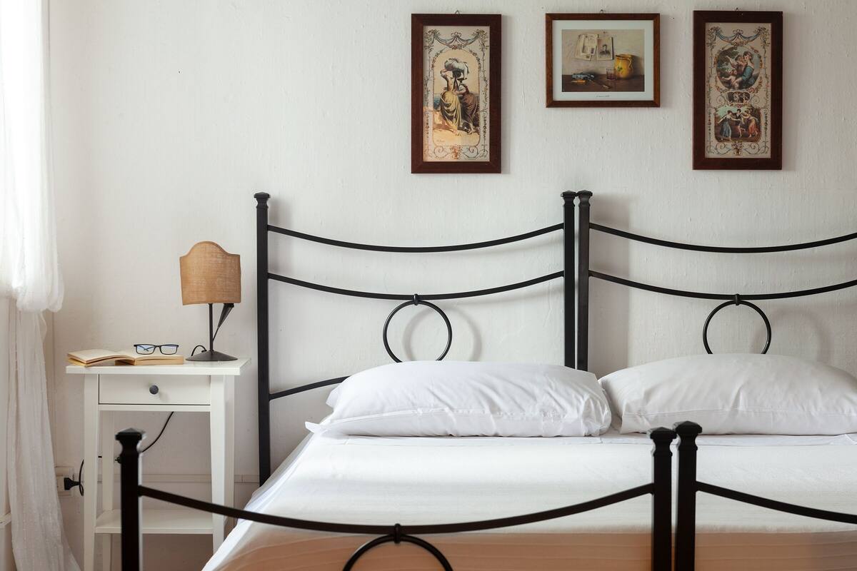 A neatly made bed with white linens, a bedside table with a lamp, and two framed artworks on the wall.
