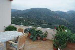 Un balcón con mesa y sillas, plantas en macetas y vistas a las montañas.