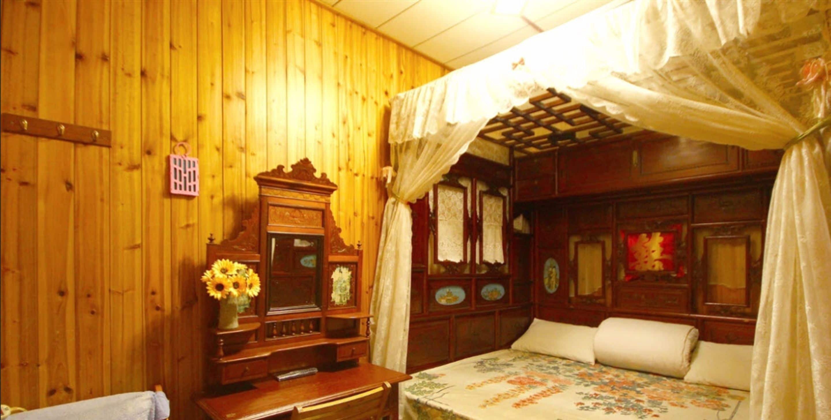 A traditional wooden room with a bed, a wooden dresser, and a vanity with a mirror.