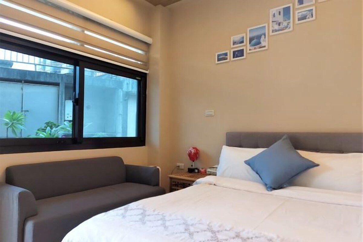 A bedroom with a bed, a sofa, a nightstand, and a window with blinds.