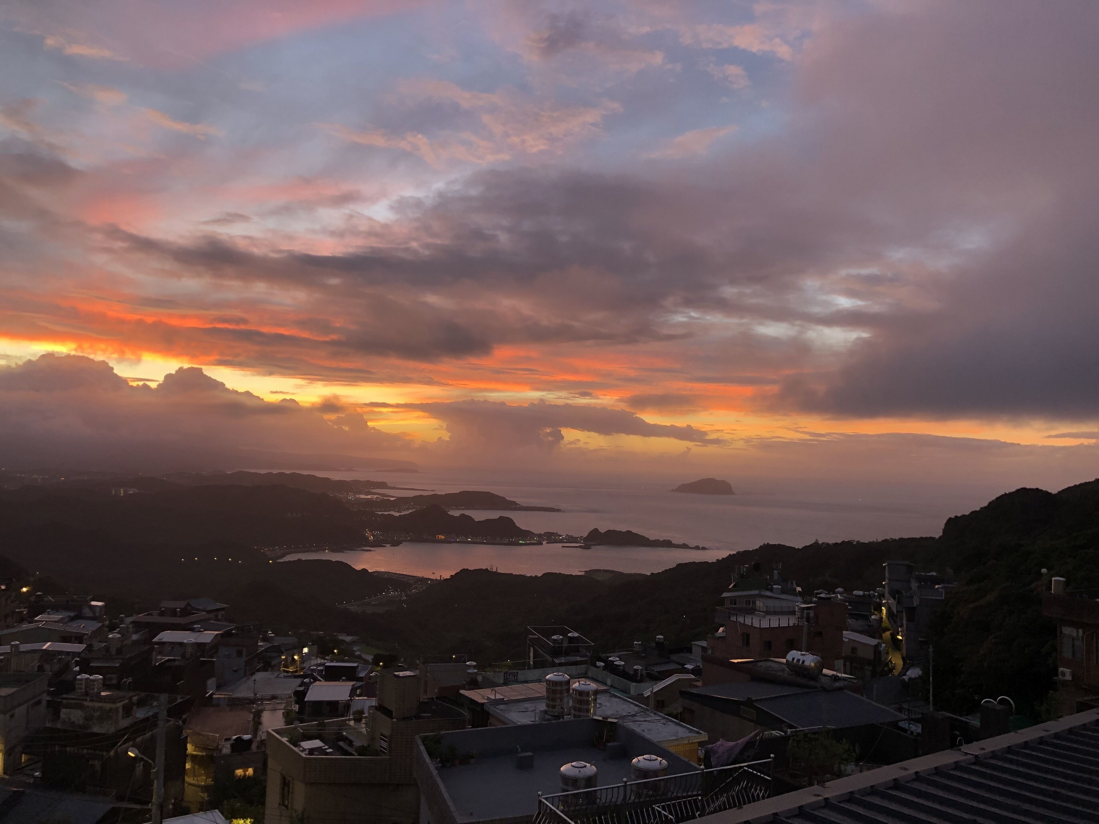 A coastal town at sunset with buildings and a view of the sea.