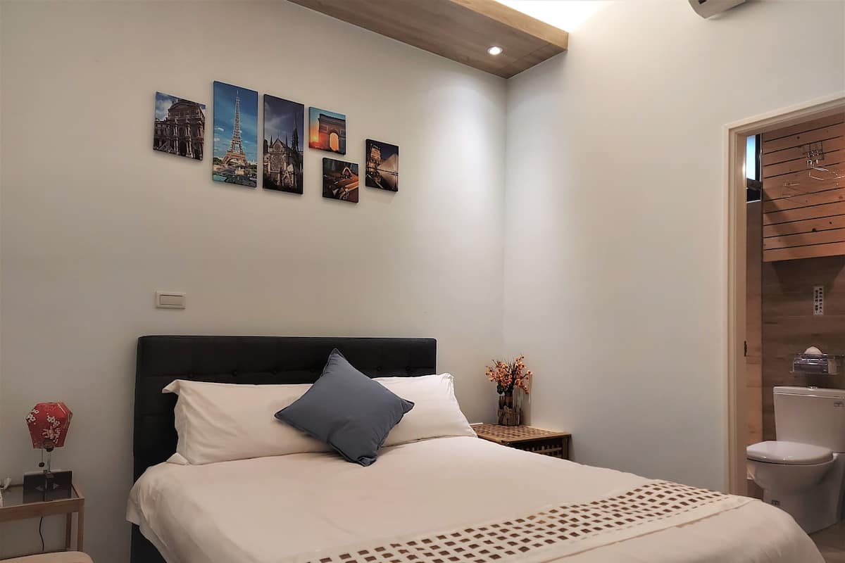 Un dormitorio con una cama, una mesita de noche, aire acondicionado de pared y una puerta de madera.