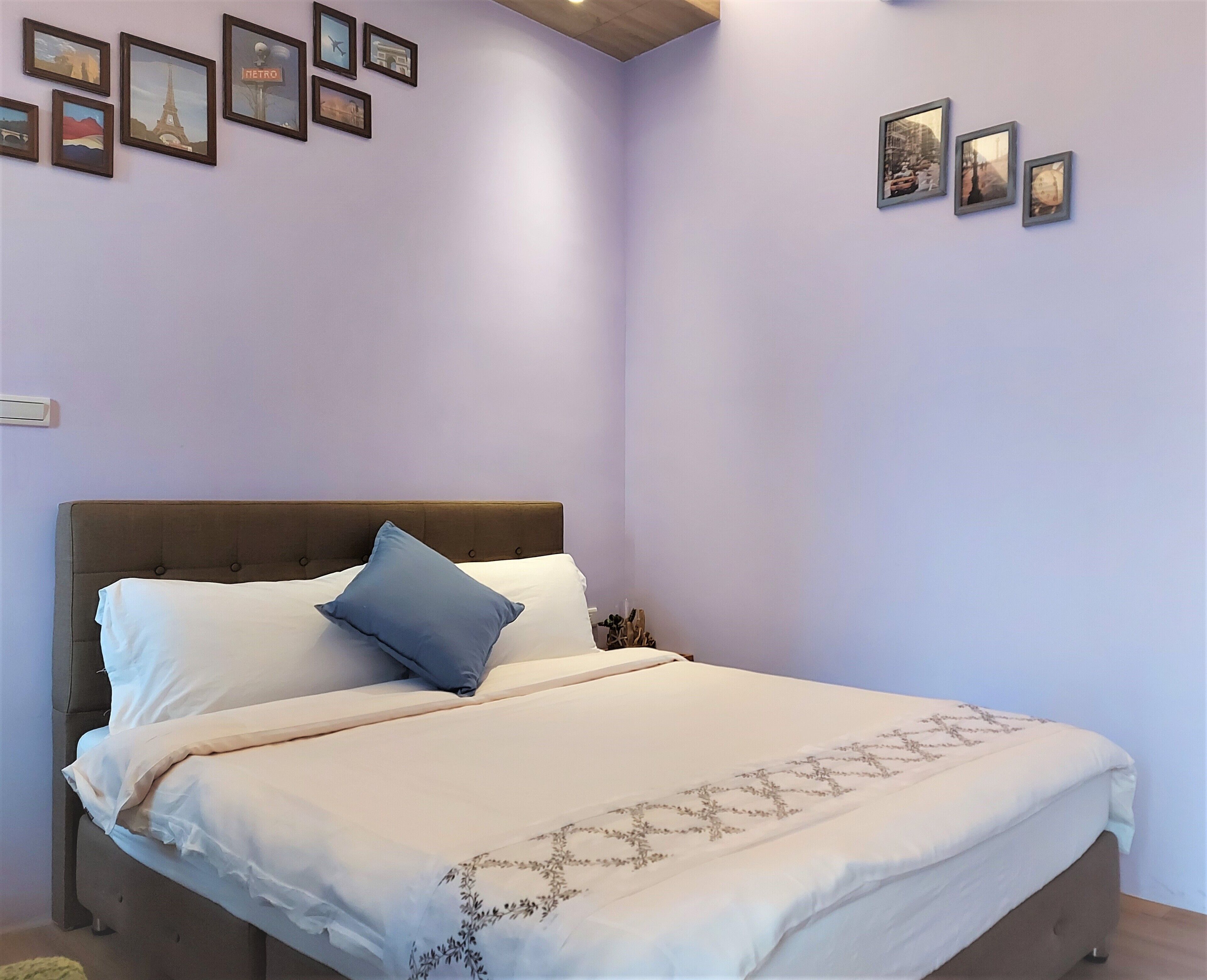 A bedroom with a bed, a headboard, and a wall with framed pictures.