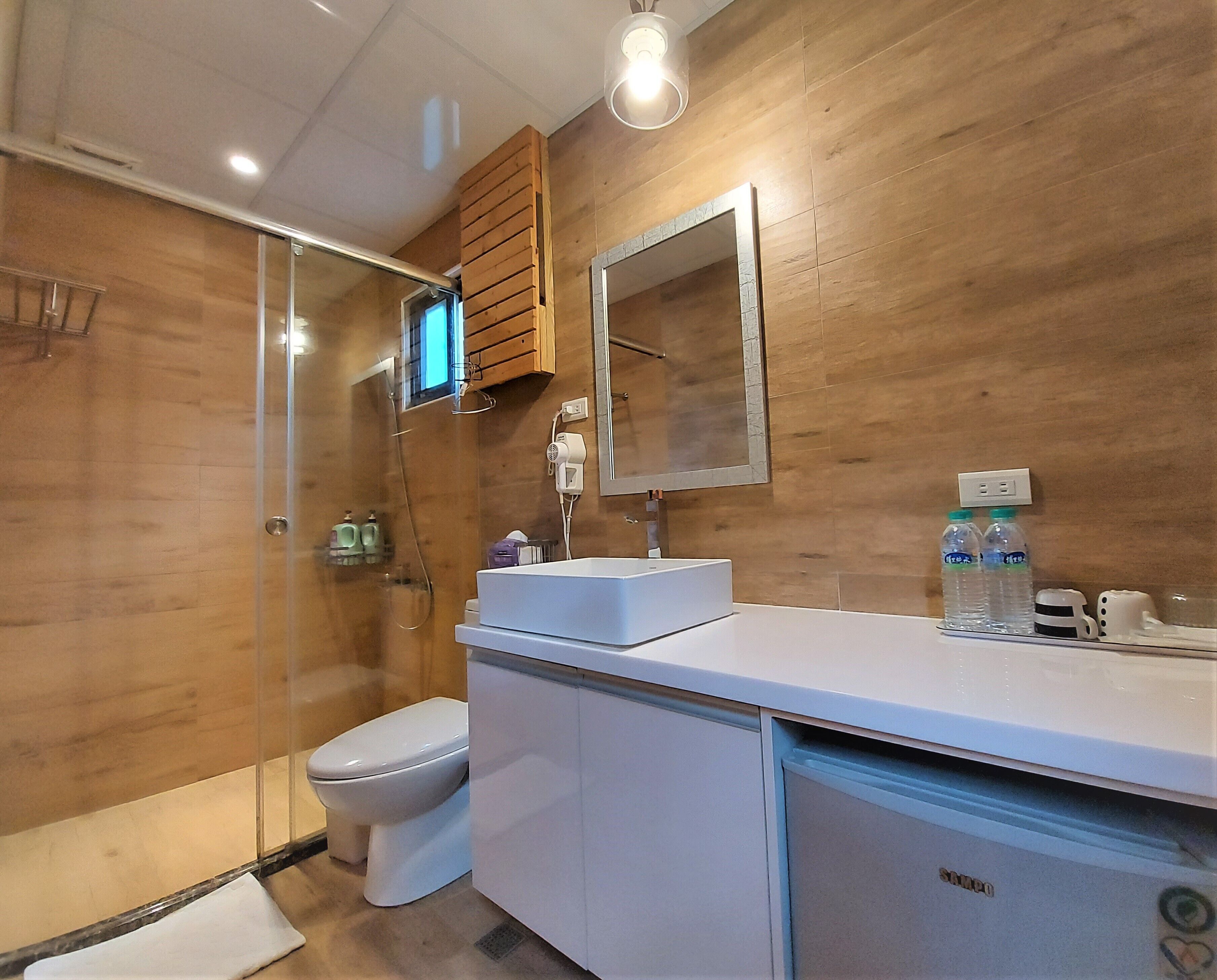 A modern bathroom with a glass shower enclosure, a white toilet, a white sink with a mirror above, and wooden wall panels.