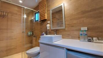A modern bathroom with a glass shower enclosure, a white toilet, a white sink with a mirror above, and wooden wall panels.