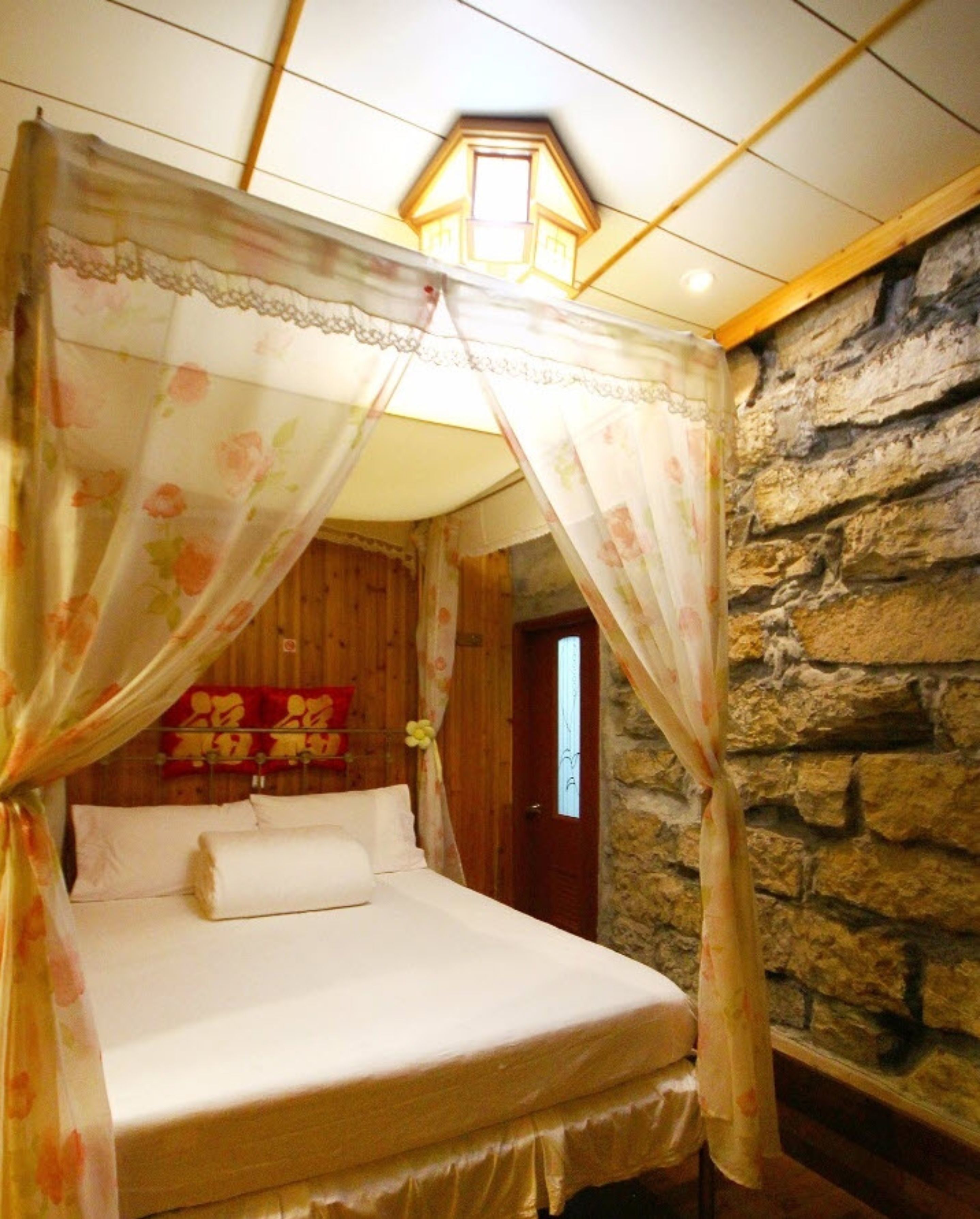 A bed with a canopy, a stone wall, and a wooden ceiling.