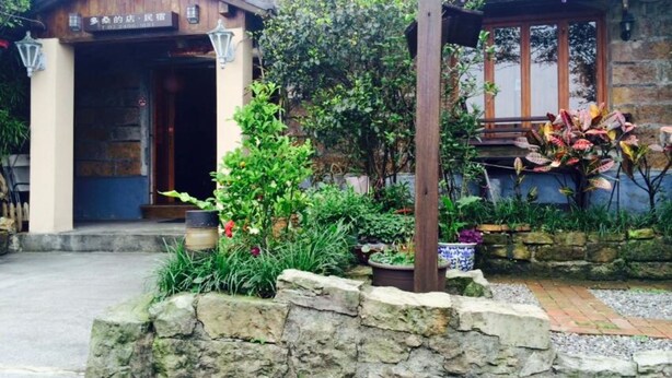 Un edificio de estilo japonés tradicional con entrada de madera y un pequeño jardín con plantas y un muro de piedra.