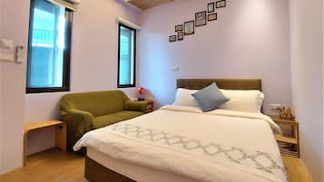 A bedroom with a bed, a green armchair, a nightstand, and a wall with framed pictures.