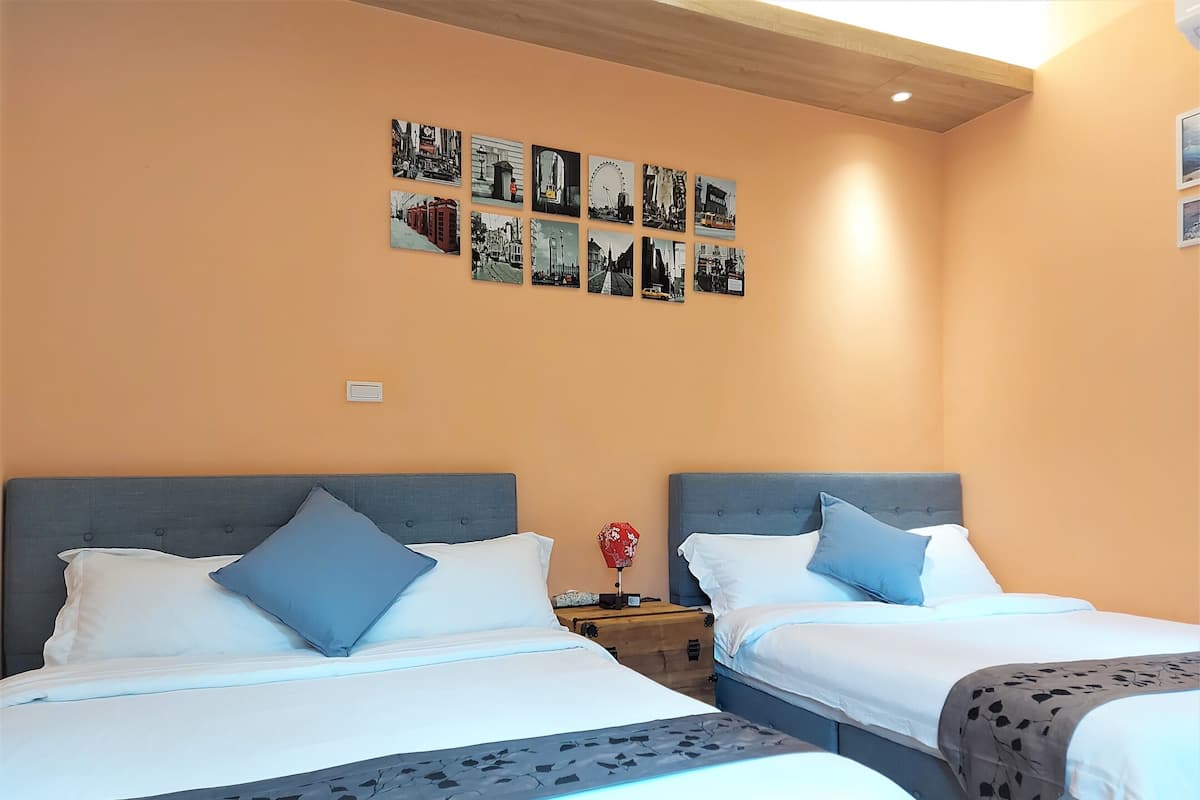 Habitación de hotel con dos camas, una mesita de noche, una pared con fotografías en blanco y negro y techo de madera.
