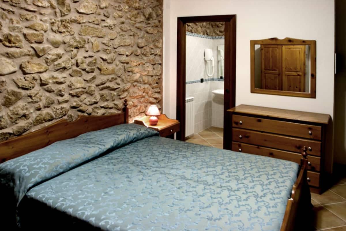 Una camera da letto con una parete in pietra, un letto di legno con copriletto decorato, un comò di legno e uno specchio appeso al muro.