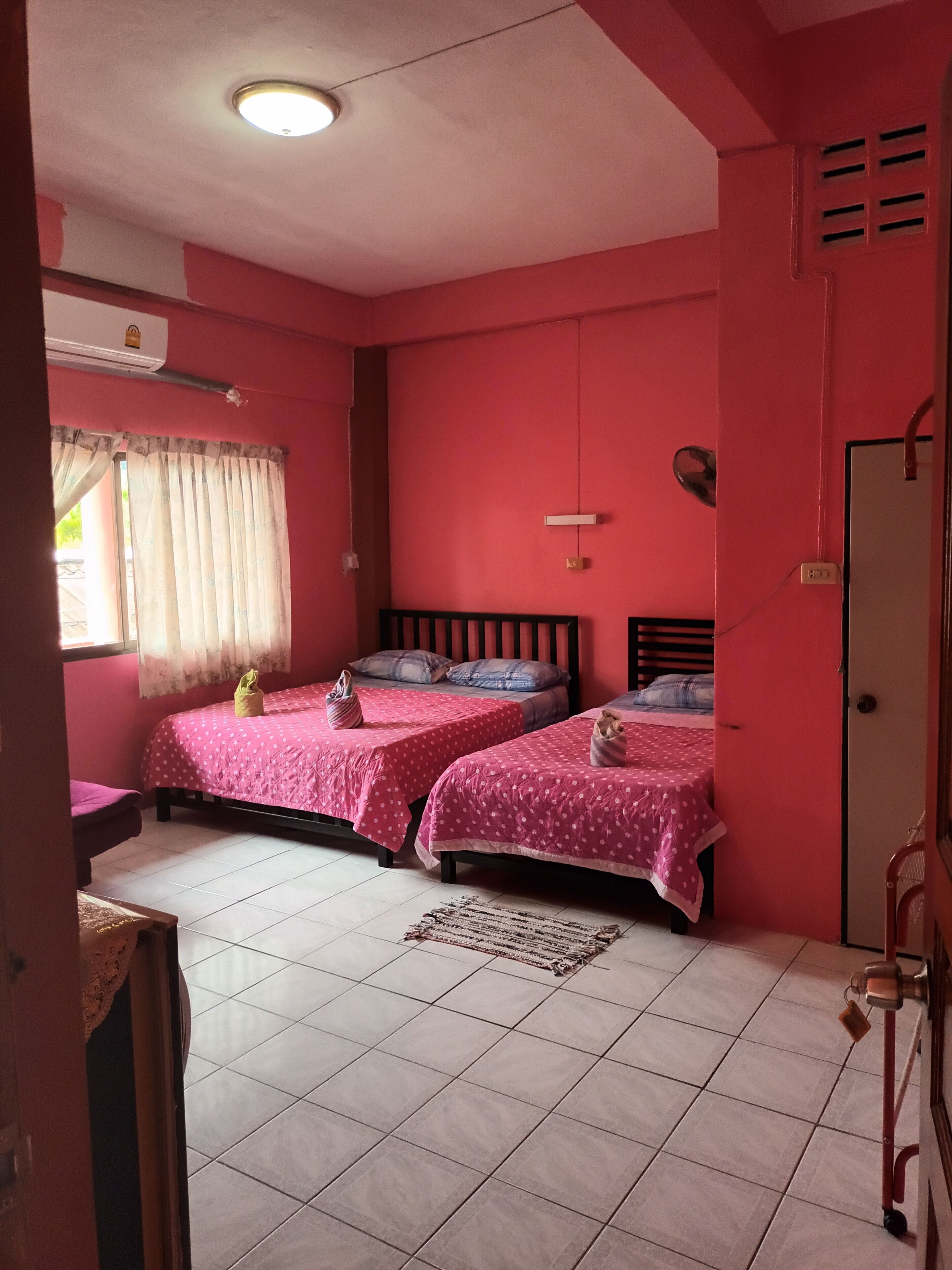 Una habitación con dos camas, una ventana con cortinas, un ventilador de techo y piso de baldosas.