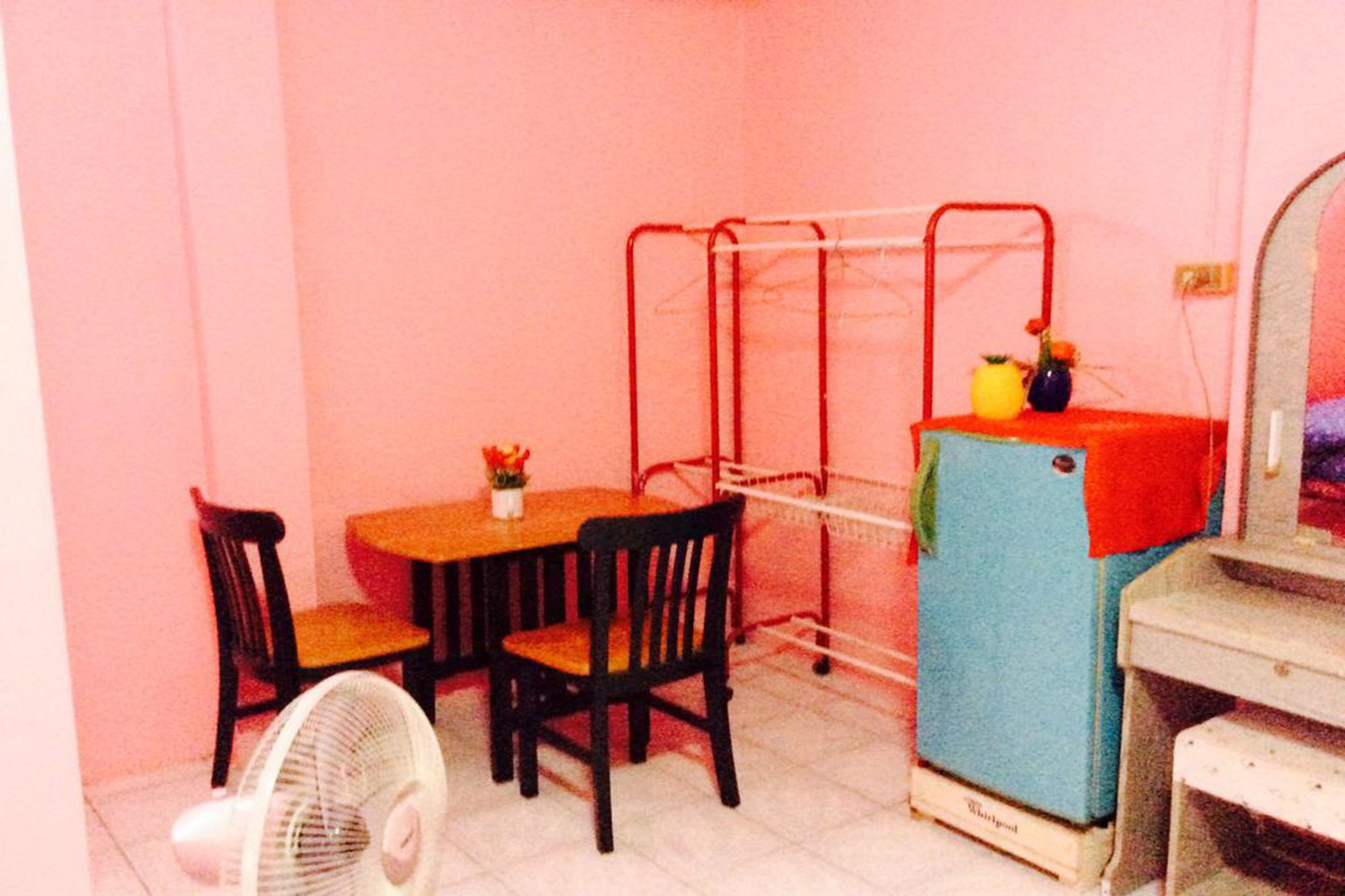 A small room with a wooden table and chairs, a fan, a red metal rack, and a blue refrigerator.
