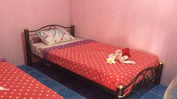 A single bed with a red polka dot bedspread and a floral pillow, placed on a blue-tiled floor in a room with pink walls.